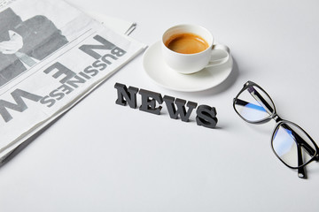 news lettering near cup of coffee, glasses and business newspaper on white