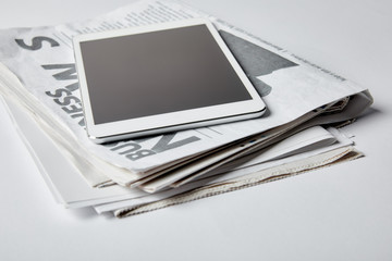 digital tablet with blank screen near business newspapers on white