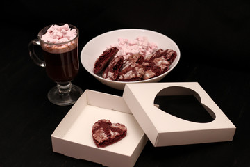 hot drink in a glass cup with pink marshmallows and white box with a transparent cover in the form of heart with cookies