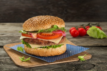 Tasty and appetising cheeseburger with tomato and green salad served on the wooden table