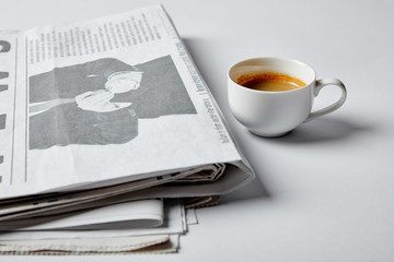 selective focus of cup with coffee near newspapers on white