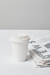 selective focus of paper cup near business newspapers on grey