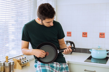 Young man in the kitchen with dripping pot like guitar.