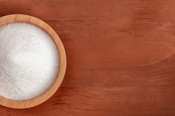 Fototapeta na wymiar A closeup of a bowl of white sugar, shot from the top on a dark rustic wooden background with copy space