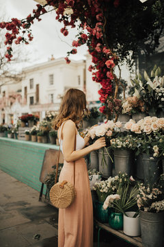 Fashionable young blogger girl holding a bunch of flowers at the flower market. Concept of blogging and street style fashion. Summer and spring outfit ideas.