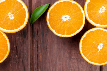 A closeup photo of fresh orange halves, shot from above on a dark rustic wooden background with a green leaf and a place for text