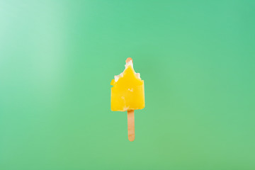 half eaten yellow popsicle on a light green background