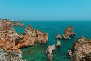 Fototapeta na wymiar Rocky cliffs and grottoes along coastline in Algarve, Portugal. Motorboat and kayaks in turquoise sea waters on a warm spring morning.