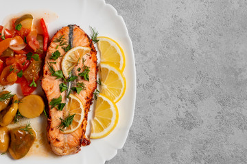 Baked salmon fillet medallion with salad of pickled vegetables and mushrooms on a white plate on a gray background, top view, flatlay, place for text, copy space