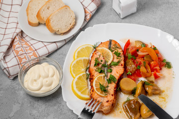 Baked salmon fillet medallion with salad of pickled vegetables and mushrooms on a white plate on a gray background, top view, flatlay