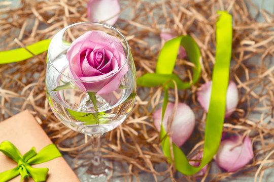 Pink rose in a glass with water and decorations on the table