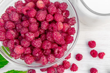 Fresh raspberries in a glass bowl and natural iogurt on a white wooden table. Healthy eating concept
