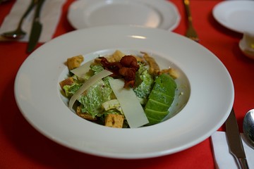 Home made caesar salad with avocado and cheese in white plate on red table.