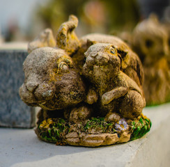 A grave sculpture of a rabbit with a baby rabbit. The statue is made of alabaster, and the rabbits are surrounded by flowers, and also sitting on grass.  