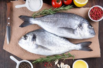 Raw fish dorado cooking and ingredients.  Dorado, lemon, tomato, herbs and spices. Top view on wood table