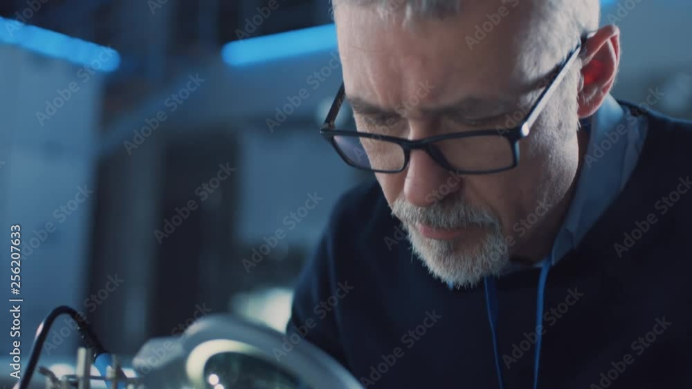 Poster electronics maintenance engineer enters his workshop with coffee beginss soldering of circuit board,