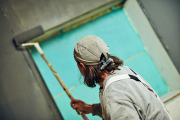 Painter painting walls with a extender roller indoors.