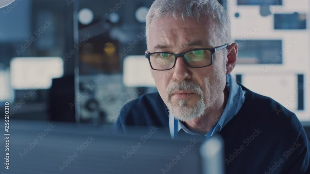 Poster portrait of handsome middle aged engineer wearing glasses works on personal computer. in the backgro