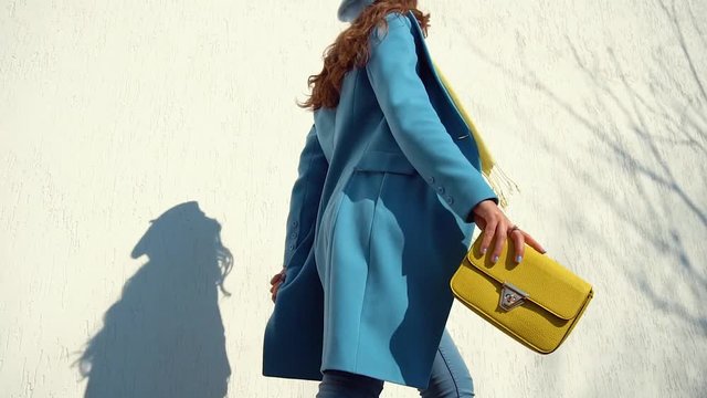 woman posing in a coat on the background of the wall with the handbag