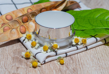White lotion jar Lotion jars with seeds and flowers around The lotion bottle is placed on the wood.