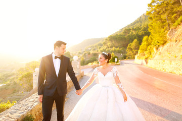 Beautiful wedding couple, bride and groom kissing and posing on road in sun