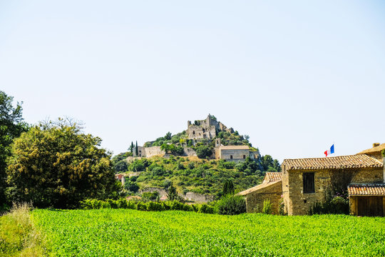 Feudal castle on the hill in the village of Entrechaux in Provence on the background of a cornfield and old buildings with a French flag. - Powered by Adobe