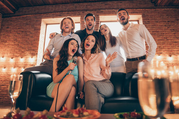 Close up photo buddies karaoke birthday company hang out shout yell scream sing she her ladies he him his guys wineglasses golden beverage wear dresses shirts formalwear sit sofa loft room indoors