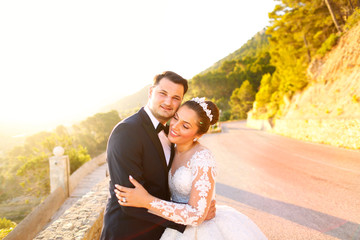 Beautiful wedding couple kissing in the sun near road and trees