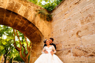 Happy wedding couple posing in park under old arch