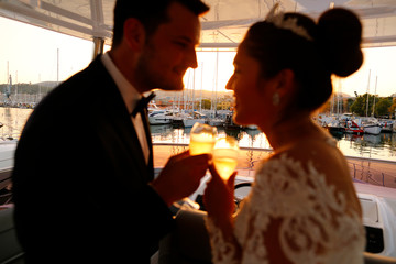 Beautiful bride and groom knock their champagne glasses in boat
