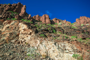 Stony cliffs on background blue sky with clouds, green foot