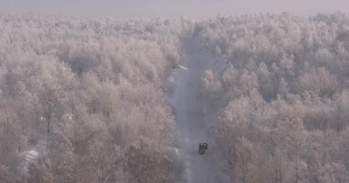 Old empty dark green truck without a trailer driving on a white snowy road through a wild forest in the mountains - Aerial drone view
