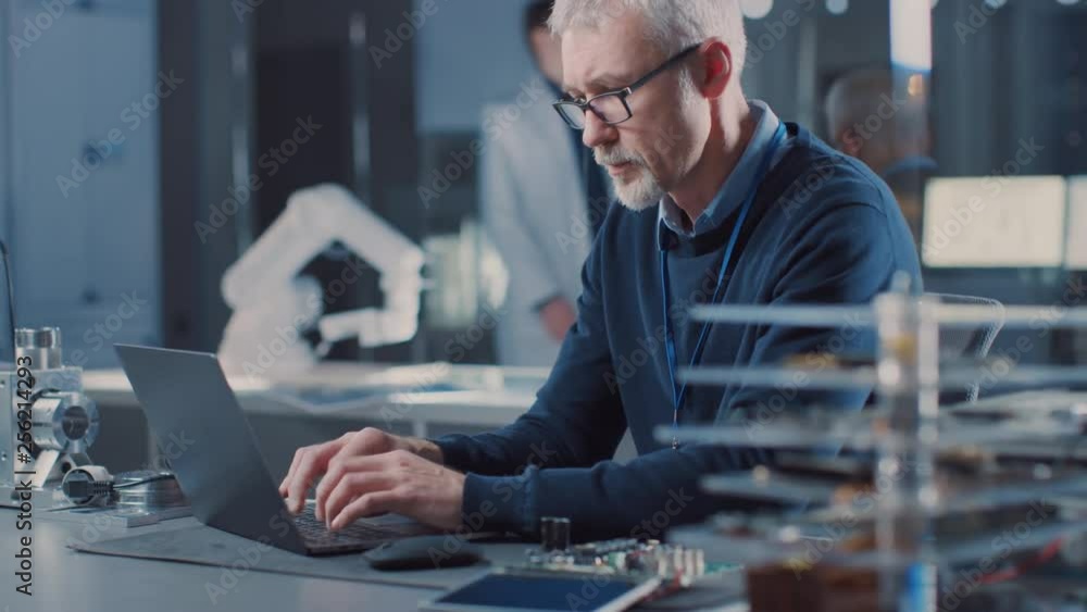 Poster professional electronics design engineer wearing glasses works on laptop computer in research labora