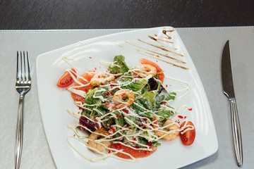 Salad with shrimps, salmon slices, tomatoes, greens on a plate on the table