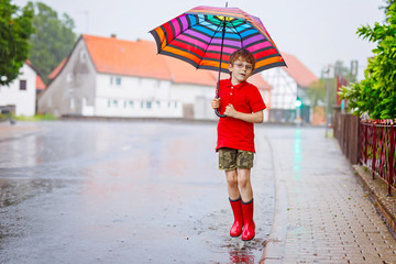 Child wearing red rain boots jumping into a puddle. Close up. Kid having fun with splashing with water. Warm heavy summer rain and happy children