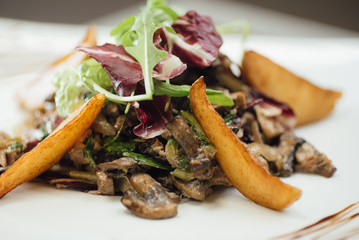 Salad with fried mushrooms, fried potatoes, greens on a plate on the table