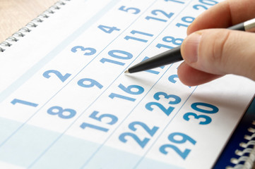 hand with a pen marks the date in the calendar