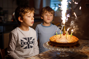 Fototapeta premium Two beautiful kids, little preschool boys celebrating birthday and blowing candles on homemade baked cake, indoor. Birthday party for siblings children. Happy twins about gifts and fireworks on tarte.