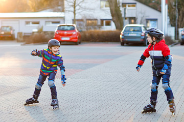 Two little kids boys skating with rollers in the city. Happy children, siblings and best friends in protection safety clothes. Active schoolboys making sports and learning to skate on inline skater.