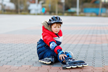 Little school kid boy skating with rollers in the city. child in protection safety clothes. Active...