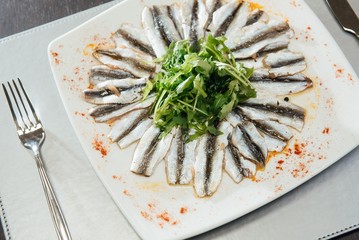 Freshly Spiced Sprat with Greens on a Plate on the Table