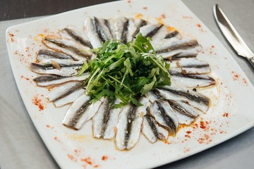 Freshly Spiced Sprat with Greens on a Plate on the Table
