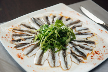 Freshly Spiced Sprat with Greens on a Plate on the Table