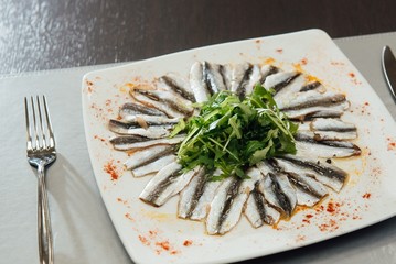 Freshly Spiced Sprat with Greens on a Plate on the Table