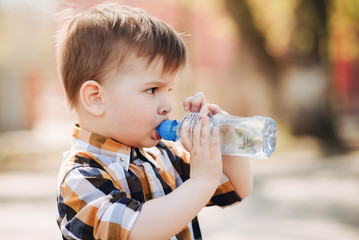 handsome boy drinks clear water from a bottle on a sunny day outside