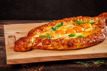 Georgian cuisine. Big khachapuri with 5 egg yolks, on a wooden board. A dish in a restaurant for a large company of people. Background image copy space
