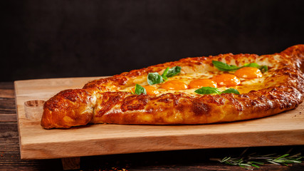 Georgian cuisine. Big khachapuri with 5 egg yolks, on a wooden board. A dish in a restaurant for a large company of people. Background image copy space