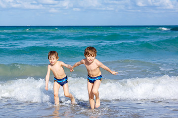 Two happy little kids boys running on the beach of ocean. Funny cute children, siblings, twins and best friends making vacations and enjoying summer on stormy sunny summer day. Miami, Florida