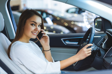 Cheerful young woman talking on the phone sitting in a car