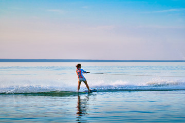 Woman surfer with red hair rolls on the board on a flat surface of water in the summer sunny evening.